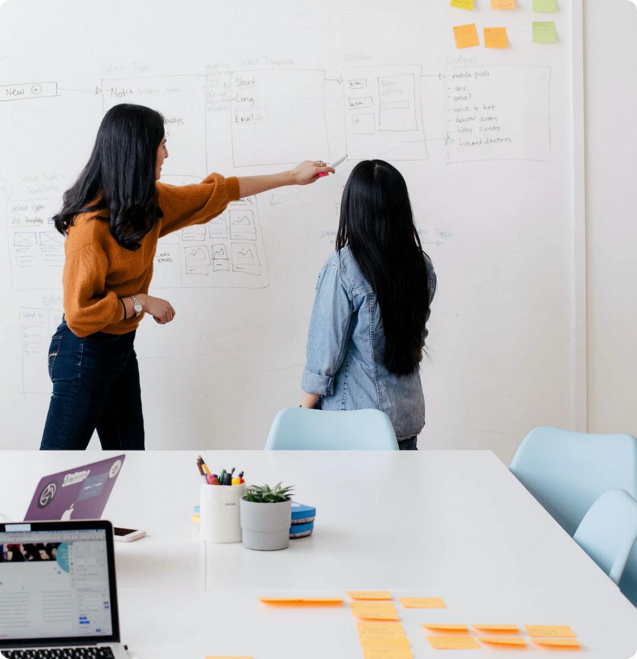 A woman showing another woman something on a whiteboard